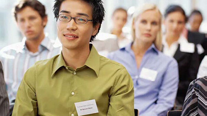 A young man with a nametag sits among a group of people