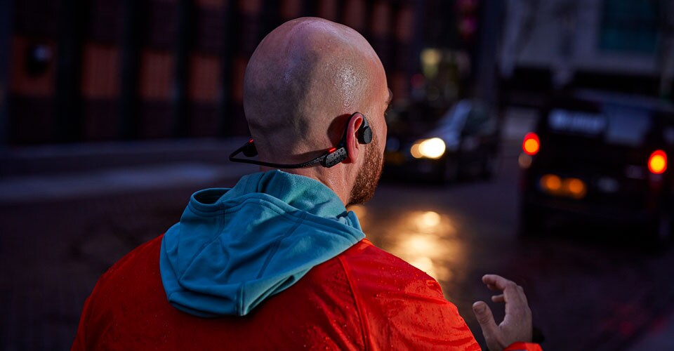 Man wearing open ear headphones on a crowded street